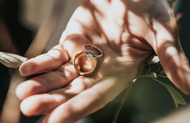 Foto de uma pessoa segurando uma aliança de namoro com anel solitário de noivado.